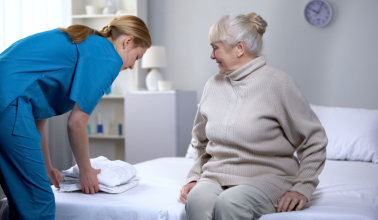 Nurse preparing clean bed-linen to female patient